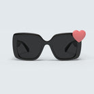 Black sunglasses against a white background show one of the Hailey collection charms: a pink heart attached to the front right side of the sunglasses.