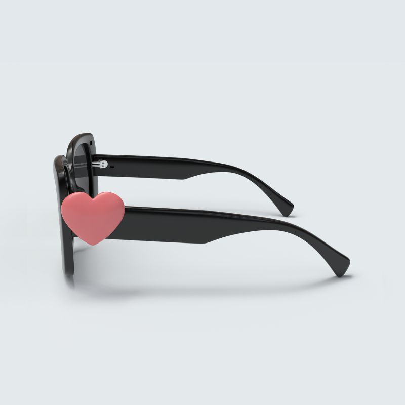 Black sunglasses against a white background show one of the Hailey collection charms: a pink heart attached to the right side of the sunglasses.